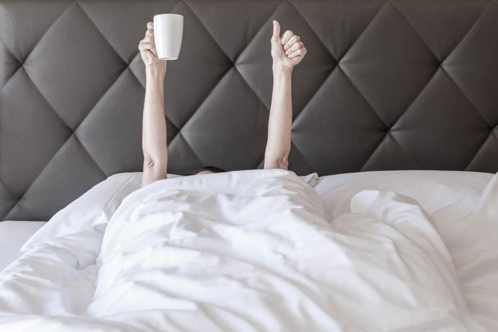 Frau im Bett hebt Hände in die Höhe